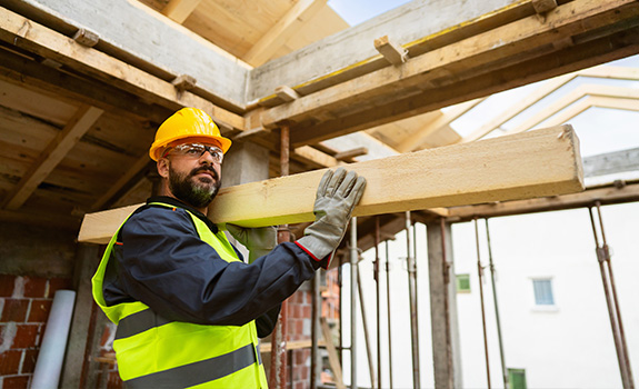 Male builder, carrying timber, while working on a construction site