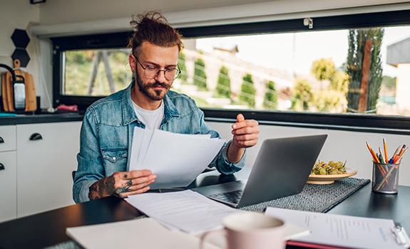 Young tradesman working at home with laptop and papers on desk