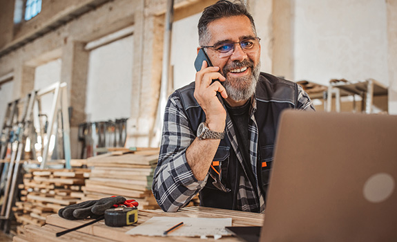 Tradesman on laptop whilst talking on mobile phone